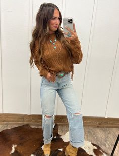 a woman taking a selfie in front of a white door wearing jeans and boots