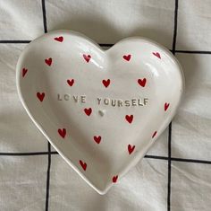 a heart shaped dish with the words love yourself written on it and small red hearts