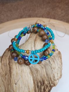 This is a triple stack boho bracelet! Each bracelet contains a different shade of blue/aqua while also incorporating some wooden beads to complete the whole Bohemian feel. You can wear these three bracelets together or you can simplify the entire look by only wearing one or two of them.  I love stackable bracelets bc each one can tell a story about the theme or purpose that the accessory is going for. This particular item reminds me of the rainforest. The wooden beads signify the trees while the greens, blues, and aquas remind us of the trees, moss, and moisture that constantly circulate the forest floors. The peace sign further signifies our abilities to protect and love both our earth and water. Hippie Friendship Bracelets With Round Beads, Turquoise Hand Wrapped Bracelets For Festivals, Bohemian Turquoise Bracelets With Wooden Beads, Hippie Turquoise Friendship Bracelets, Hippie Beaded Wrap Bracelet, Turquoise Hand-wrapped Hippie Beaded Bracelets, Hippie Turquoise Hand-strung Bracelets, Turquoise Hippie Friendship Bracelet, Hippie Turquoise Friendship Bracelet