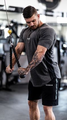 a man with tattoos on his arm and arms holding a rope in the middle of a gym