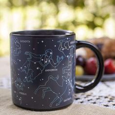 a black coffee mug sitting on top of a table next to some fruit and bread