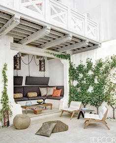 an outdoor living room with white walls and wooden furniture on the floor, surrounded by greenery