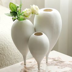 three white vases with flowers in them on a table