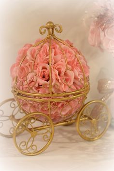 a pink flower in a gold carriage with wheels