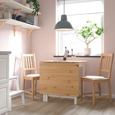 a kitchen with pink walls and wooden chairs in front of a counter top, potted plant on the window sill