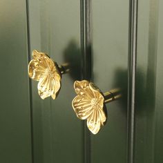 a pair of gold flower shaped door knobs on a green front door with black handles