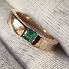 a gold ring with an emerald stone in the center on a white cloth, close up