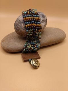 This beautiful One- of- a -Kind southwest style beaded bracelet is adorned with beautiful Picasso beads of varying colors of gold,  turquoise blue, smoky blue, brown, soft green, and burgundy.  The larger beads are 4 m. m.  Bohemian mix Opaque Picasso . The small ones are size 6 Aged Striped Czech Glass Rocaille seed beads.  The ends of the bracelet are finished with tan leather with a bronze southwest style button.  This bracelet is 7 inches long and 1 inch wide. This bracelet will fit 6-7 inch inch wrist .   I hope that you will love this very stylish bracelet!   ENJOY! Artisan Beaded Multicolor Wrap Bracelet, Artisan Multicolor Beaded Wrap Bracelet, Earthy Turquoise Bracelets For Festival, Bohemian Cuff Bracelet With Large Beads, Bohemian Adjustable Cuff Bracelet With Large Beads, Adjustable Bohemian Cuff Bracelet With Large Beads, Hippie Bracelet With Colorful Beads, Brown Beaded Southwestern Jewelry, Hippie Brown Bracelet With Colorful Beads