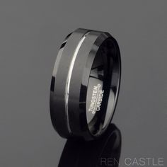 a black and white wedding band with an engraved logo on it, sitting on a reflective surface