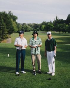 three men standing on top of a lush green field next to a golf ball hole