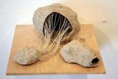 a sculpture made out of rock and grass on top of a wooden board with a white wall in the background