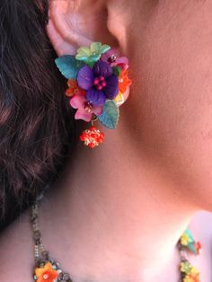 Gorgeous little petunia earring with a central purple polymer clay flower mixed with a striking color combo of red, orange, green and yellow. These earrings are hand sewn together with glass beads and hand painted resin flowers, finished off with a pretty handbeaded bauble. This is a quality piece of jewelry that will last a life time. Created by designer Colleen Toland who has been creating her unique style of vintage jewelry for more than 30 years. All of our pieces come with an engraved tag w Whimsical Multicolor Flower Shaped Jewelry, Multicolor Flower-shaped Jewelry With 3d Flowers, Multicolor 3d Flower Shaped Jewelry, Adjustable Multicolor Earrings With Flower Charm, Adjustable Multicolor Flower Charm Earrings, Whimsical Multicolor Flower Jewelry, Whimsical Multicolor Flower Charm Earrings, Handmade Colorful Flower Earrings, Red Flower-shaped Polymer Clay Jewelry