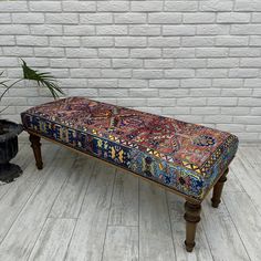 a bench sitting on top of a wooden floor next to a brick wall and potted plant