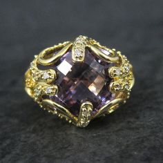 This stunning estate ring is gold vermeil over sterling silver. It features a faceted amethyst, estimated to be around 6 carats, accented by genuine diamonds. The face of this ring measures 5/8 of an inch north to south with a rise of 9mm off the finger. Size: 8 The designers hallmark is JH but I cannot seem to identify who that is. Condition: Flawless Formal Gold Amethyst Ring With Diamond Accents, Elegant Yellow Gold Amethyst Ring With Gemstone Accents, Heirloom Amethyst Ring With Accent Stones For Formal Occasions, Heirloom Amethyst Ring With Accent Stones For Formal Events, Formal Amethyst Diamond Ring With Gemstone Accents, Gold Amethyst Diamond Ring With Center Stone, Gold Amethyst Jewelry With Diamond Accents, Elegant Jewelry With Gemstone Accents, Elegant Amethyst Ring With Gemstone Accents For Anniversary