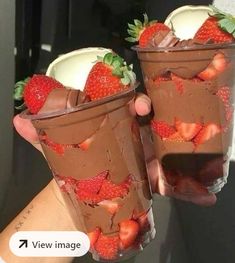 two cups filled with chocolate and strawberries on top of each other, one being held up by someone's hand