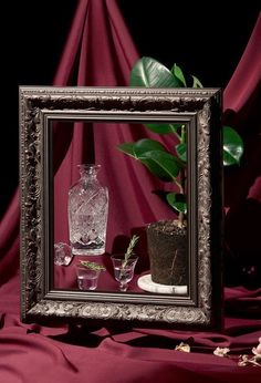 there is a vase and two glasses in front of a framed mirror on a table