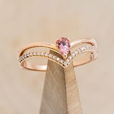 a pink diamond ring sitting on top of a piece of wood with diamonds around it