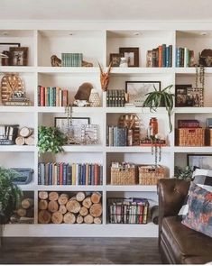 a living room filled with lots of books on top of a white book shelf next to a brown leather chair