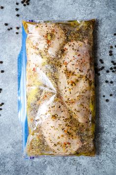 a plastic bag filled with chicken and seasoning sitting on top of a gray surface