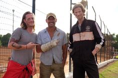 three men standing next to each other near a fence