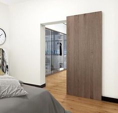 a bedroom with a bed, clock and wooden flooring in front of a white wall