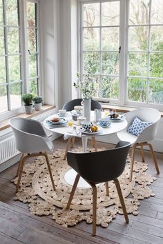 a dining room table with chairs and plates on it in front of large open windows