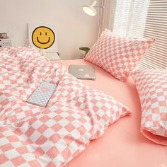 a bed with pink and white checkered sheets, pillows and a laptop on it