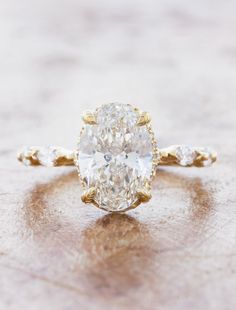 an oval cut diamond ring with three small diamonds on the band, set in 18k yellow gold