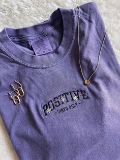 POSITIVE VIBES ONLY! super trendy embroidered tshirt! pair it with your favorite denim shorts or leggings. floral design with self love quote 💜 get summertime fine with a pop of color!  This T-Shirt is available in 5 colors: Ash Gray, Grape Purple, Emerald, Wine, and Carribean Blue. If there is a color you have in mind other than the ones available, send me a message and I can help! -Sweatshirt brand: Comfort Colors -Sizes available: Adult Small - Adult 2XL -Fit: slightly oversized fit - I'd su Trendy Crew Neck T-shirt With Embroidered Text, Trendy Embroidered Summer T-shirt, Spring Streetwear Tops With Letter Embroidery, Casual Letter Embroidery T-shirt For Streetwear, Spring Tops With Letter Embroidery For Streetwear, Trendy Short Sleeve Tops With Letter Embroidery, Trendy Crew Neck T-shirt With Letter Embroidery, Trendy Purple Tops With Letter Print, Spring Letter Embroidery Top For Streetwear