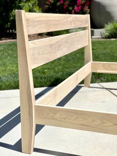 a wooden bed frame sitting on top of a cement floor next to a lush green field