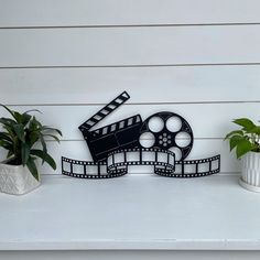 a black and white photo of a movie camera on a shelf next to potted plants