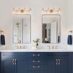 two sinks and mirrors in a bathroom with blue cabinets, gold pulls and brass knobs