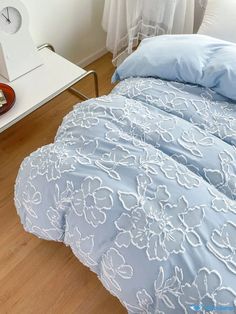 a blue comforter with white flowers on it next to a clock and nightstands