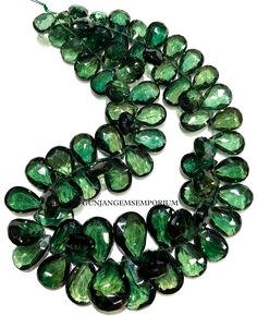 green faceted glass tears are arranged in a circle on a white background with the word