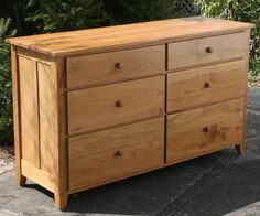 a wooden dresser sitting on top of a cement floor next to trees and bushes in the background