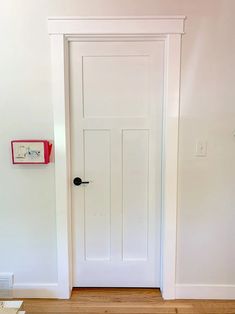 an empty room with a white door and wood flooring on one side and a red box on the other