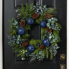 a christmas wreath with blue ornaments and greenery hangs on a black front door,