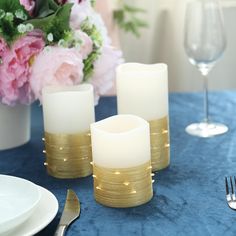 three lit candles sitting on top of a blue table cloth next to plates and silverware