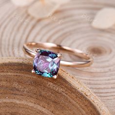 a pink and blue ring sitting on top of a piece of wood with flowers in the background