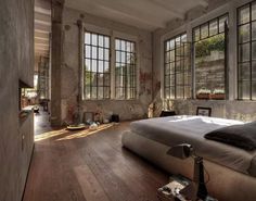 a large bedroom with wooden floors and windows on the wall, along with a bed