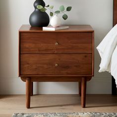 a wooden dresser with two vases on top of it and a bed in the background