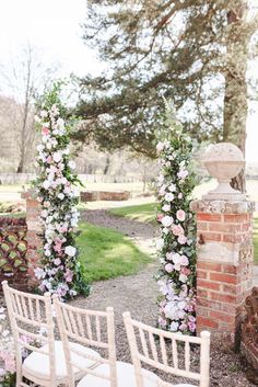 an outdoor ceremony setup with white chairs and pink flowers on the arch, surrounded by greenery