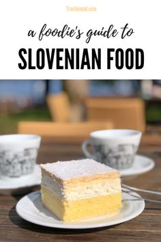 a white plate topped with a piece of cake next to two cups and saucers