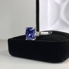 Beautiful Tanzanite* & White Sapphire Ring * 2.25ct Emerald Cut Violet Blue Tanzanite* measures 9mm x 7mm * 3.5mm Brilliant Cut White Sapphire Accents * 2.5cts Total weight * 14k White Gold * Size 9 Hallmarked & Gift Ready! Matching Earrings & Pendant Necklace is also Available! *Tanzanite is one of very few gemstones that cannot be grown in a Lab, however, these Laboratory Grown Simulate Stones are optically identical to a natural Tanzanite in color and are just as hard but, do not Blue Radiant Cut Lab-created Sapphire Jewelry, Radiant Cut Tanzanite Jewelry With Prong Setting, Radiant Cut Lab-created Sapphire Jewelry, Tanzanite Ring With Radiant Cut Center Stone, Gift Emerald Cut Tanzanite Sapphire Ring, Brilliant Cut Tanzanite Gemstones For Gift, Brilliant Cut Tanzanite Gemstones As Gift, Radiant Cut Tanzanite Jewelry Gift, Radiant Cut Tanzanite Ring With Center Stone