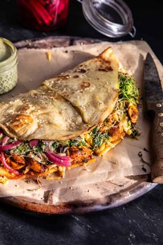 a burrito sitting on top of a paper plate next to a jar of sauce