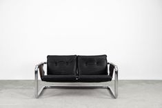 two black leather couches sitting next to each other on concrete floor with white wall in the background