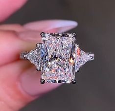 someone is holding an engagement ring with three princess cut diamonds