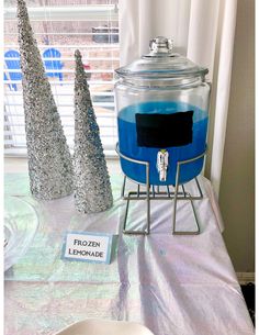 there is a blue liquid in a glass container on a table next to two silver trees