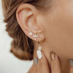 This set consists of four separate earrings, in three different styles, all made from sterling silver and embellished with zirconia stones. It has: 🌟 One stud earring with four tiny zirconia arranged in a flower shape; 🌟 One stud earring with three marquise-cut zirconia arranged in a fan shape with one small round zirconia hanging beneath; 🌟 One pair of huggie hoop earrings with a flower shaped charm hanging from their lower edge, decorated with six round zirconia. A feminine and elegant set 3 Piercings Ear Studs, Jewelry Wedding Earing Multi Holes, Earrings 3 Lobes, Flower Shaped Earrings With Diamond Accents, Flower Earrings With Diamond Accents In Cubic Zirconia, Fine Jewelry Flower Earrings, Pierced, Fine Jewelry Flower Pierced Earrings, Huggie Earrings Gold, Golden Jewelry