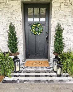 a front door with two lanterns and a wreath on the entrance mat next to it